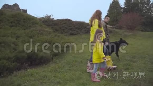 秋天，美丽的高加索母亲、小女儿和十几岁的儿子与大黑人杜伯曼漫步的侧面景色