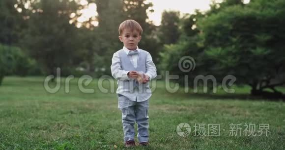 可爱的小男孩穿着一件绿色的衣服在中央公园的一块绿色的田野里，在镜头前吃着零食