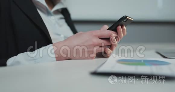 在办公室背景下一个女人手里拿着一部手机的特写镜头。 年轻女子使用智能手机