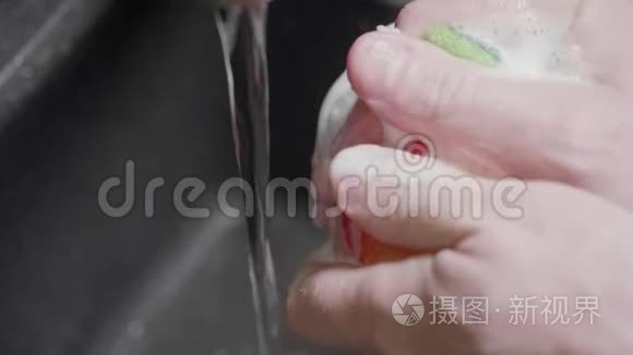 男人用海绵把红苹果放进水槽里。 清洗水果时使用清洁用品