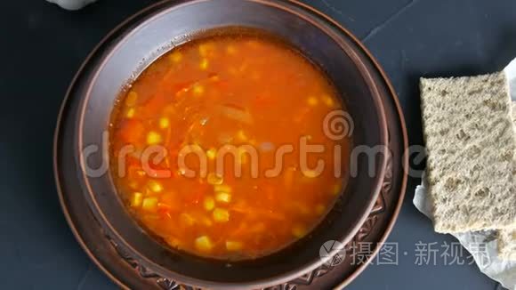 热红番茄素食汤，蔬菜和玉米在一个黑色背景的粘土老式盘子的顶部视图。