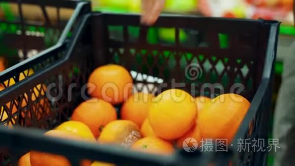 超市里的一个女人从一个盒子里拿出橘子放进一个袋子里。