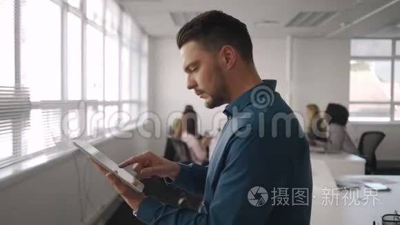 一位专业的年轻商人正忙于使用数码平板电脑，而他的同事则在办公桌前工作