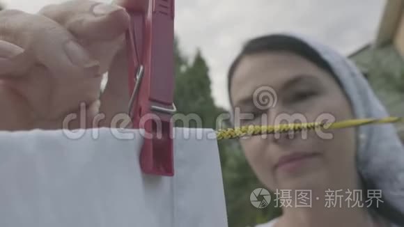 漂亮的高级妇女，头上披着白色披肩，在晾衣绳上挂着白色的衣服，在户外晾衣针