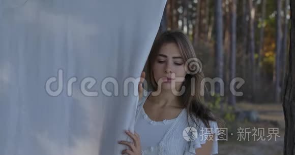 一位年轻美丽的高加索女人站在森林里环顾四周的肖像。 穿着白色衣服的漂亮女孩