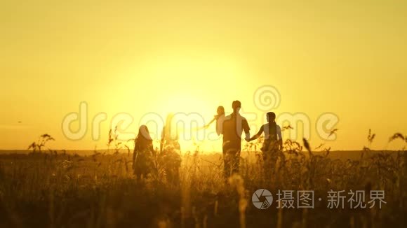 幸福家庭的观念.. 幸福的大家庭在夕阳下穿过田野。 父母和三个孩子走进来