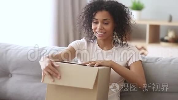 快乐的非洲女人顾客打开纸板箱坐在沙发上