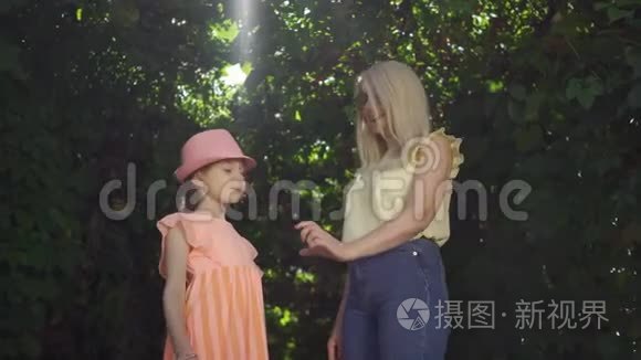 可爱成熟的金发母亲和她漂亮的女儿在夏天的花园或公园里用手指做心形