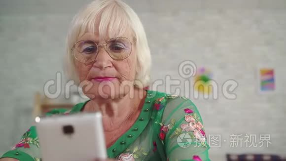 头发灰白的老年妇女使用智能手机，坐在靠近客厅的桌子旁