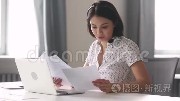 微笑着的亚洲商界女性戴着耳机，一边说话一边看着笔记本电脑