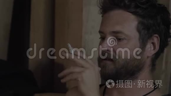 在室内一个没有灯光的地方，一个长着漂亮蓝眼睛有魅力的留着胡子的家伙在室内抽烟。 4k. 4k