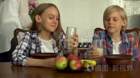 可爱的男孩和女孩喝透明眼镜的牛奶。 小兄弟在餐桌旁享用健康的饮料