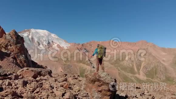 徒步旅行者背着背包站在山上的一块大石头上