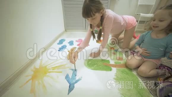 两个女孩在地板上用水彩颜料和画笔在一张大画纸上画画，孩子们共同的创造力。