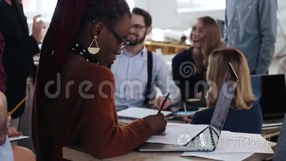 美丽的非洲年轻女性在笔记本电脑上工作，快乐的多民族商务人士在办公室背景。