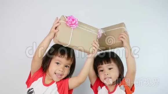 快乐的亚洲小女孩和她的妹妹拿着一个用回收纸包装的礼品盒，孤立在白色背景上。