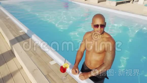 英俊的非洲男人在游泳池里喝鸡尾酒