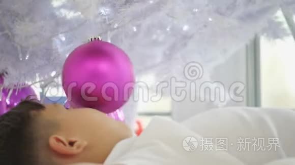 歪歪扭扭的视频，小孩子躺在圣诞树下，玩着粉红色的球。