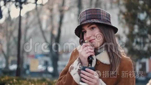 一个戴着帽子的黑发美女正在喝咖啡，在一条城市街道上摆姿势