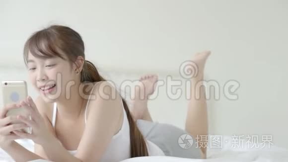美丽的肖像年轻的亚洲女人微笑着躺着看智能手机阅读社交网络与享受床上卧室