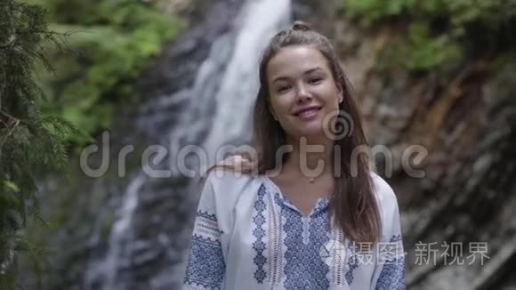 一幅年轻女子的肖像，她的脸上有雀斑，看着瀑布前面的相机。 女孩花时间