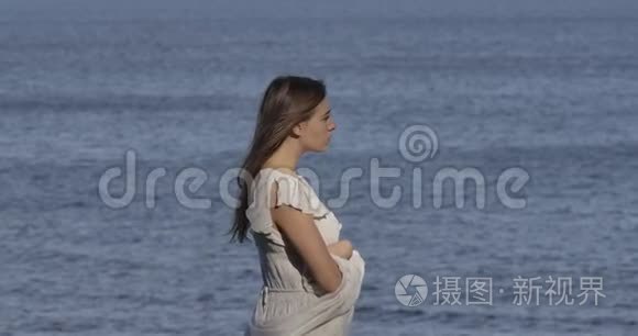 站在海浪背景下思考着一位穿着浅色白裙的白种人美丽女子的侧面景色