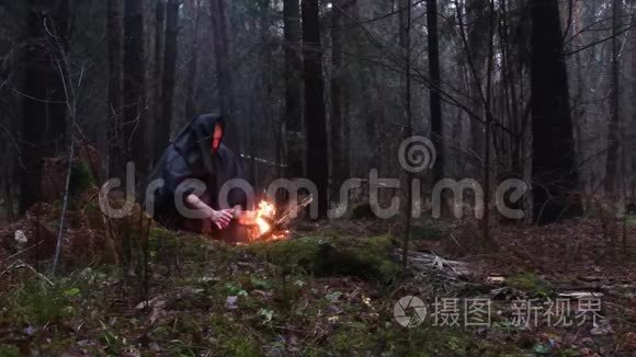 一个穿着黑色长袍的老和尚正在黑暗的秋林中用火取暖。