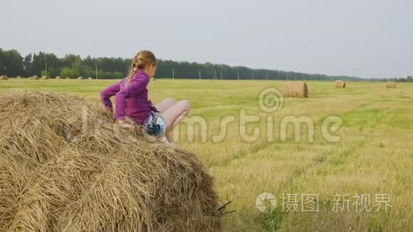 农场干草堆上的快乐少年女孩。 微笑的女孩在乡间田野上竖起大拇指。 干草秸秆