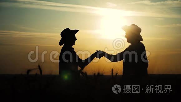 农业耕作两个农民团队合作，在一片土地上握手红脖子，在日落时检查小麦作物。 男性农民