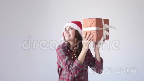 快乐美丽的女人戴着圣诞帽和睡衣摇动礼盒。 假日概念。 慢动作