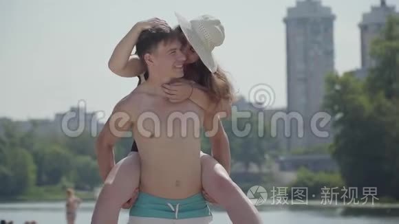 快乐的年轻夫妇在海滩上玩得很开心。 那个女孩坐在一个男人的背上微笑。 情侣们在附近享受周末时光