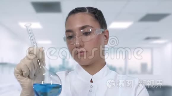 一位女实验室技术人员在玻璃瓶中检查一种蓝色液体，并在一个科学实验室进行临床研究。 关闭