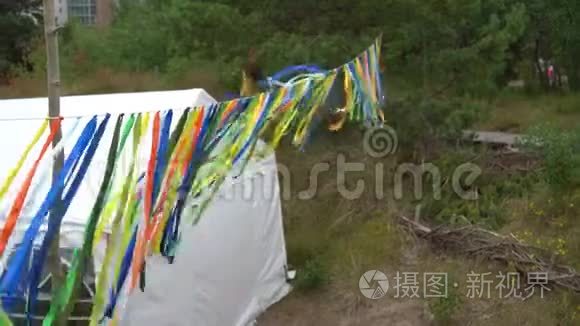 五颜六色的丝带挂在派对帐篷附近，人们在大自然中散步