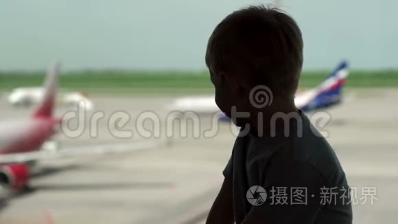 小男孩的剪影靠近机场的窗户，他看着飞机。