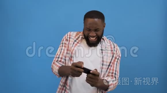 赢得比赛。 兴奋的非洲男人庆祝成功，使用智能手机超过蓝色背景，复制空间4