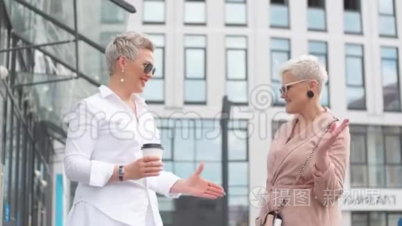 两位商务女士站在现代办公楼的背景上握手