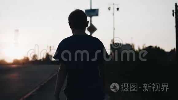 日落时男孩的酷画片。 那个男孩沿着海滨散步。 摄像机跟着他。