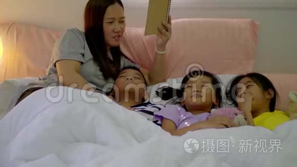 年轻的母亲和她的女儿女孩和儿子在家里的卧室里读一个故事。
