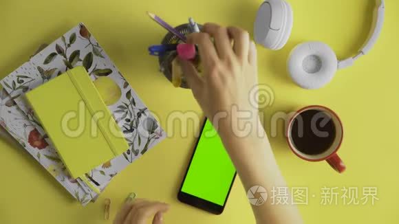 女士使用智能手机，黄色桌子背景上有绿色屏幕。