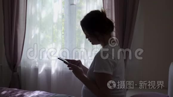 穿着白色T恤的孕妇拿着电话坐在床上