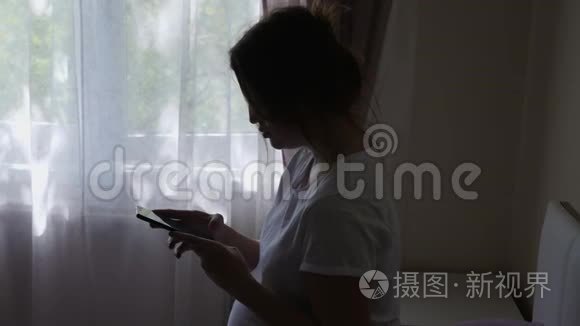 穿着白色T恤的孕妇拿着电话坐在床上