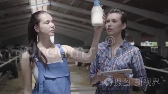 肖像两名专业可爱的女农民工人在奶牛场检查牛奶瓶的质量。 一个