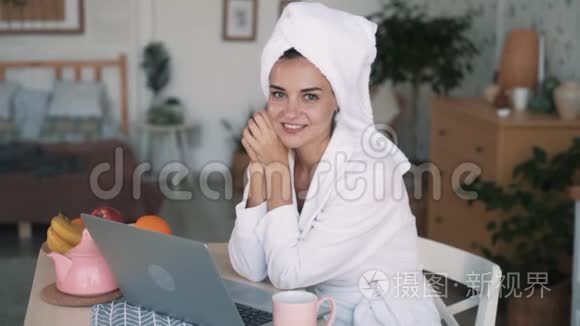 头上戴毛巾的女孩坐在厨房里，手提电脑，看着相机，微笑，慢动作