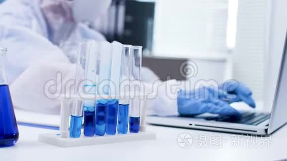关闭科学家在她的笔记本电脑上打字和在试管中吸烟的蓝色液体