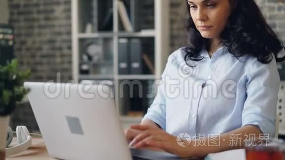 疲惫的年轻女士用笔记本电脑打字和在工作场所打哈欠的肖像