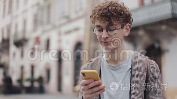 年轻的戴眼镜的学生使用他的现代手机设备与朋友聊天，打字在屏幕上站立