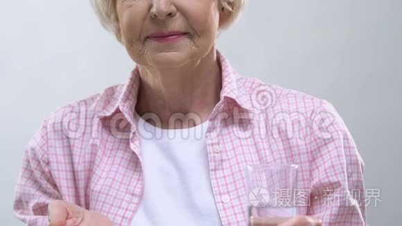 微笑的老年妇女在镜头前出示药丸和一杯水，医疗保健