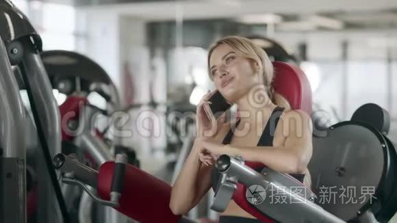 开朗的女人在体育健身馆的健身训练机上讲手机。