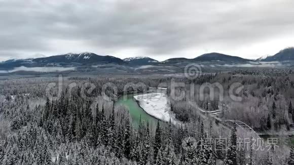 在一个寒冷的冬日，无人机照相机穿过一片茂密的森林，带着一个翠绿的池塘和一条靠近山脉的公路