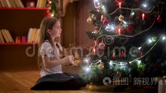 房间里坐在地板上的可爱女孩装饰了一棵带球的圣诞树